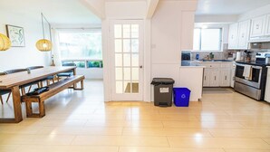 Een moderne keuken met witte kastjes, een houten eettafel en een blauwe afvalcontainer.