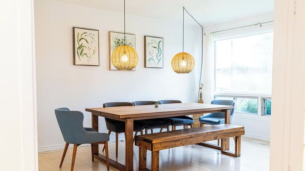Een eetruimte met een houten tafel, blauwe stoelen, een bank en hangende lampen.