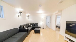 Een moderne woonkamer met een hoekbank, een flatscreen televisie en een vloerlamp.