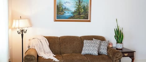 A living room with a wooden ceiling, a sofa, a coffee table, a lamp, a painting, and a potted plant.