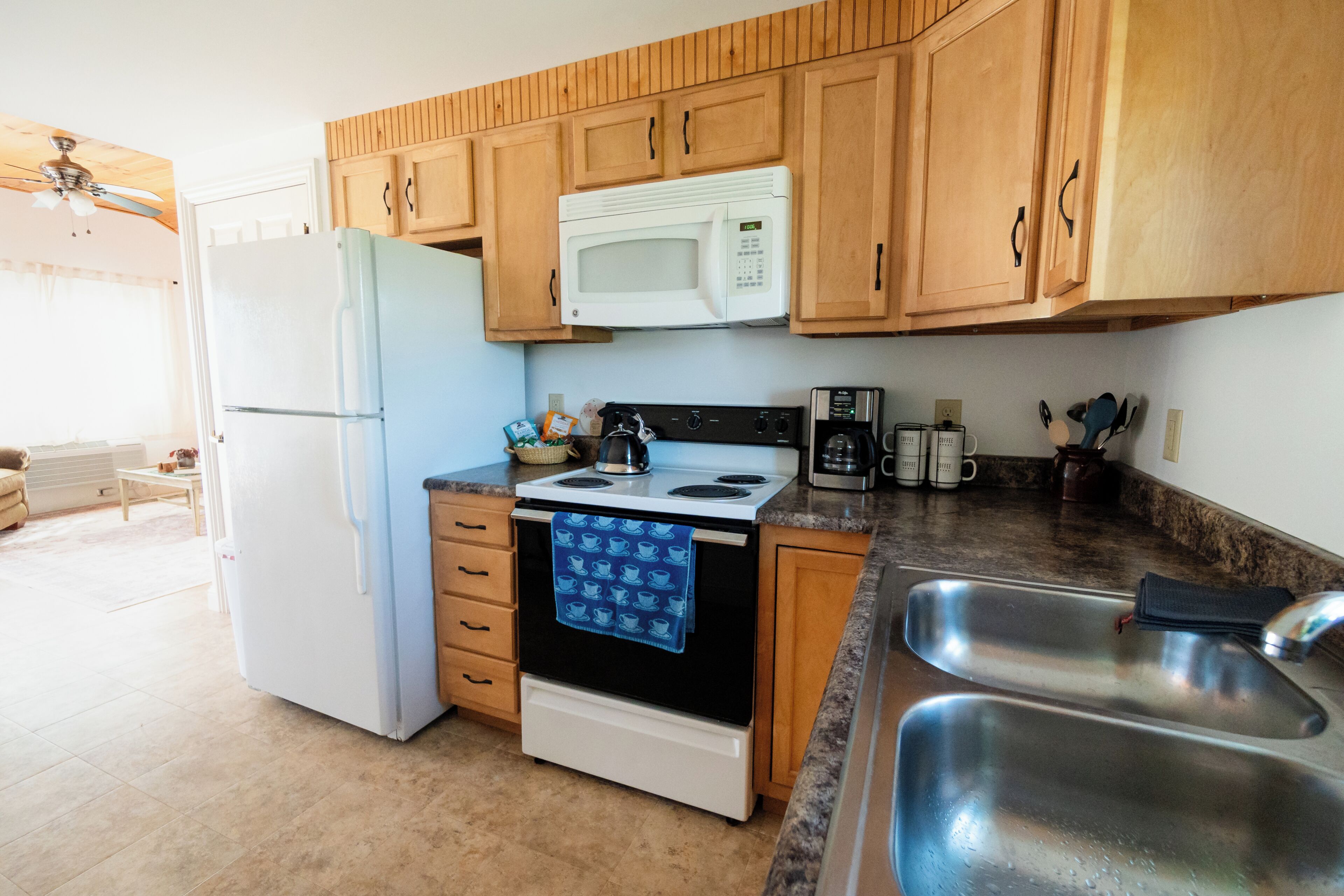 Una cocina con armarios de madera, un microondas blanco, una estufa, un fregadero y un refrigerador.
