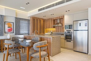 A modern kitchen with a central island, built-in appliances, and a dining area with patterned chairs. - VESTA  - Luxury APT - 2BR - Zayed City (II) (Sheikh Zayed City)