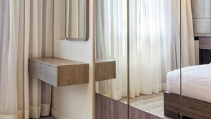 Un dormitorio con un armario de madera, una mesita de noche, un espejo y cortinas translúcidas.