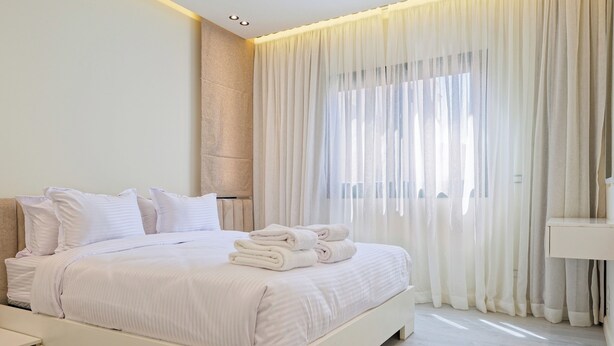 Een moderne slaapkamer met een groot bed, witte beddengoed en een raam met dunne gordijnen.