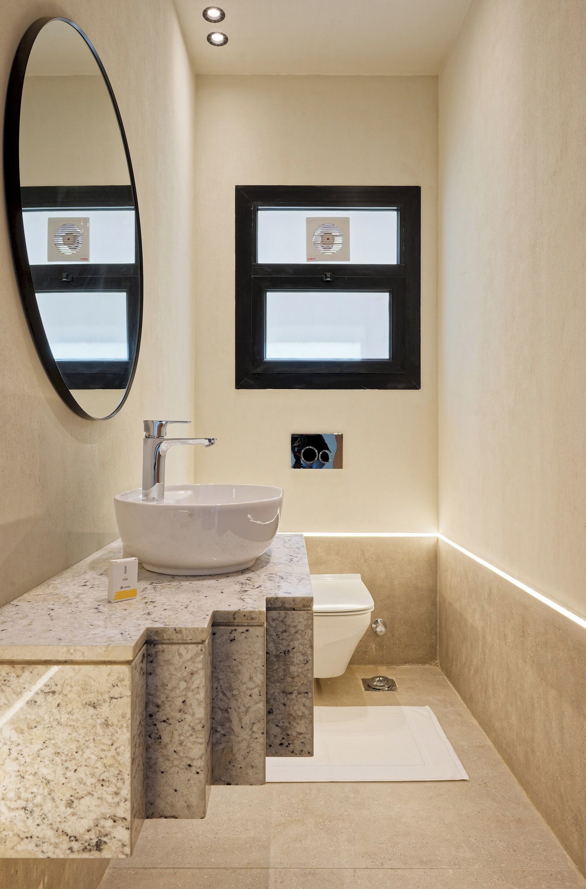 Une salle de bain avec un lavabo blanc, un miroir, une fenêtre et des toilettes.