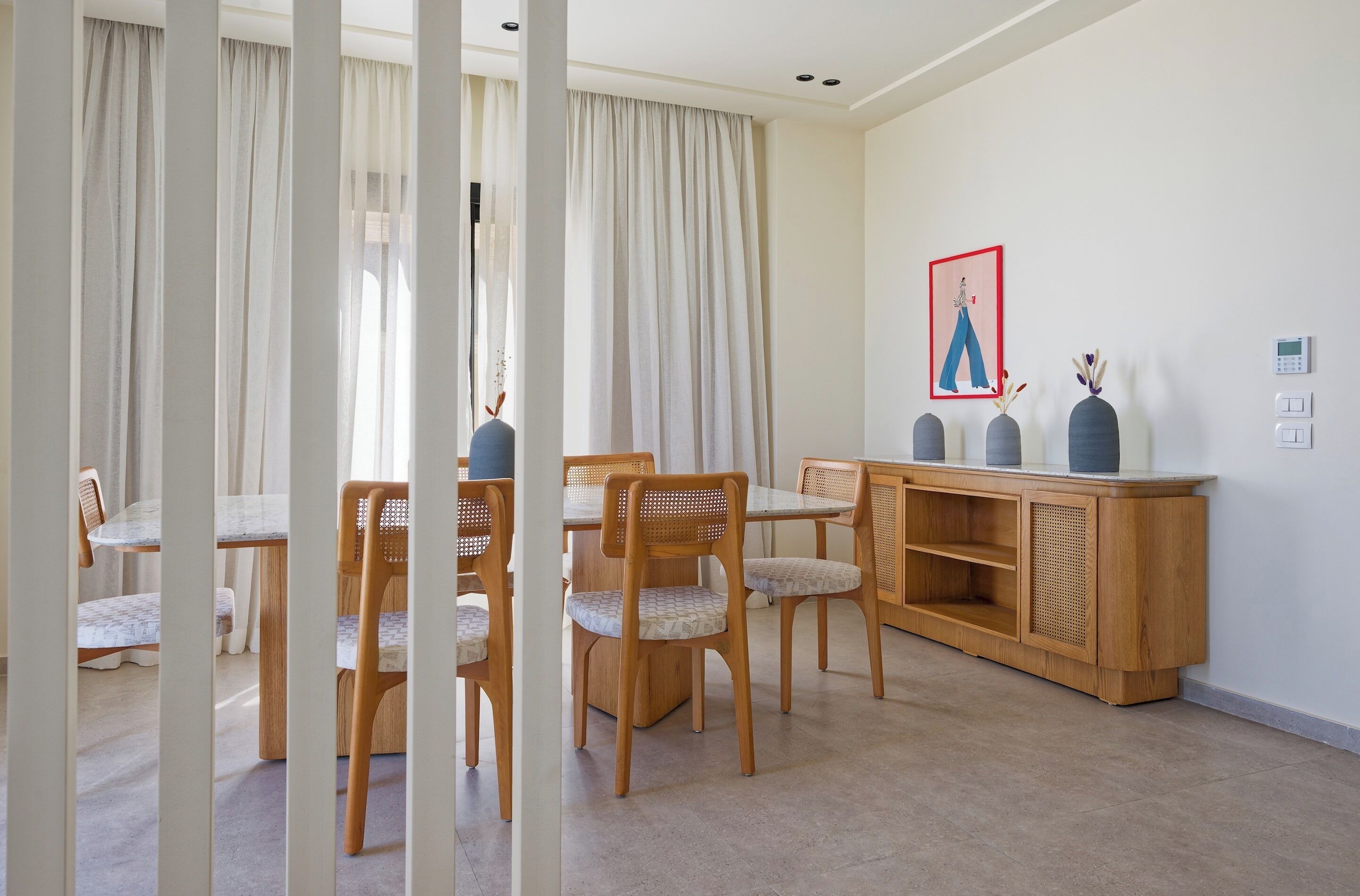 Un coin repas avec des chaises en bois et une table en marbre, un meuble en bois orné d’objets décoratifs, et un interrupteur fixé au mur.