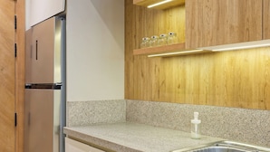 Een moderne keuken met een roestvrijstalen koelkast, een granieten aanrechtblad, houten keukenkastjes en een inbouwkast met potten.
