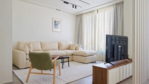Een moderne woonkamer met een hoekbank, een groene fauteuil, een houten salontafel, een flatscreen televisie en een decoratief wandobject.