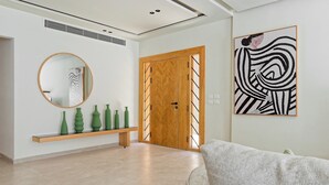 Un interior moderno con una puerta de madera, un espejo redondo y una estantería con un florero verde.