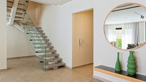 Un interior moderno con una escalera de cristal, una puerta de madera y un espejo redondo en la pared.