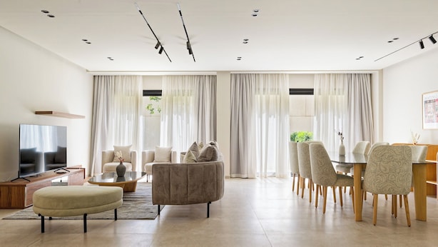 Una sala de estar moderna con sofá, reposapiés, televisor y comedor con sillas y una mesa.