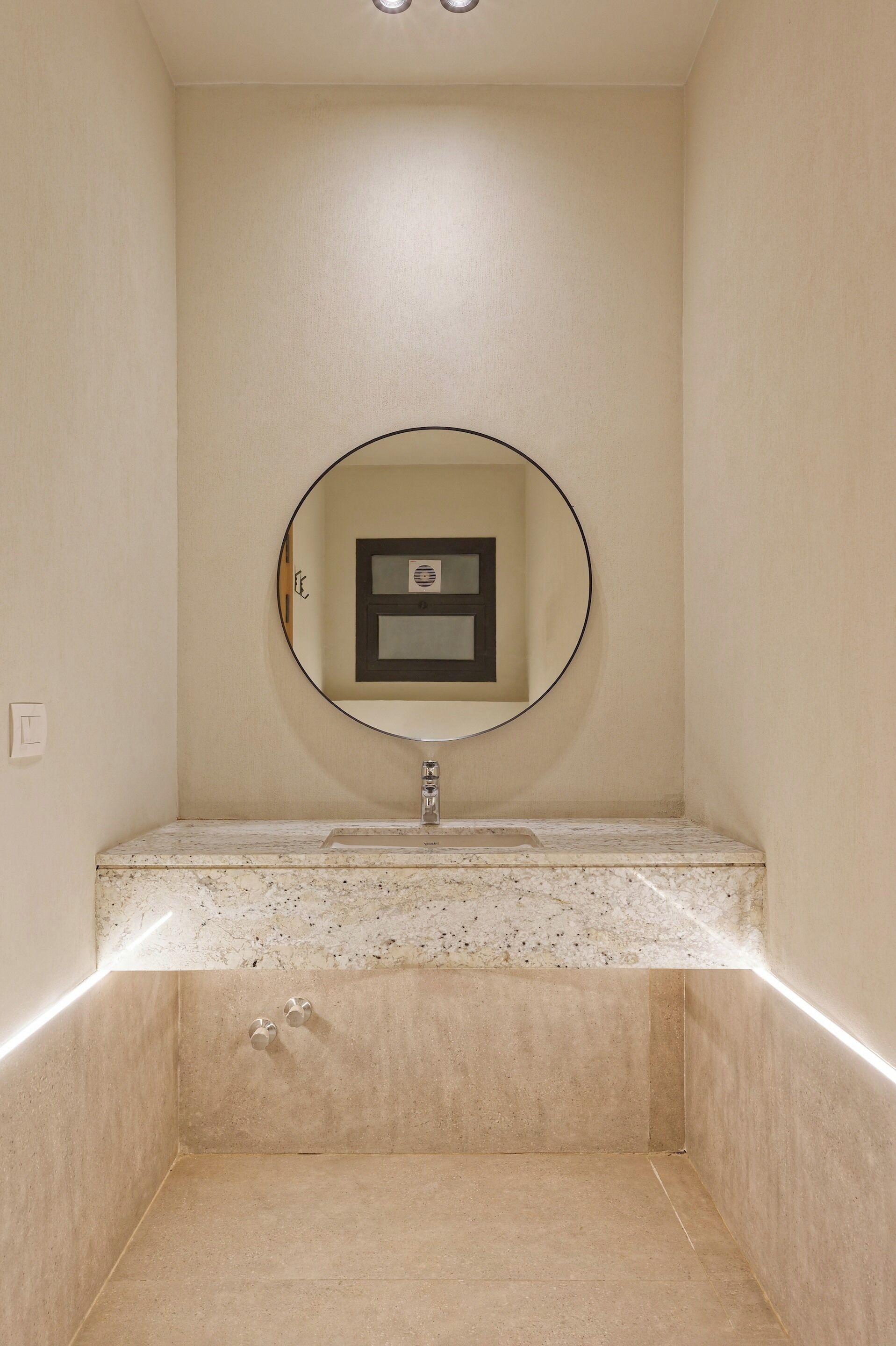 A bathroom with a round mirror, a framed picture, and a marble countertop.
