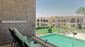 Un balcón con sillas y vistas a una piscina y edificios.