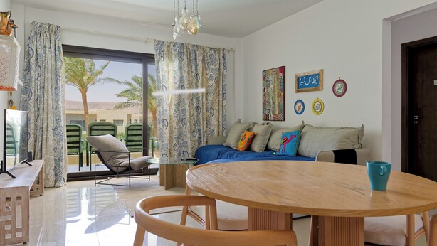 Una sala de estar moderna con un sofá, una mesa de comedor y vistas a palmeras al exterior.