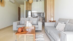 Ein modernes Wohnzimmer mit einem grauen Sofa, einem Holztisch und einer Küche im Hintergrund.