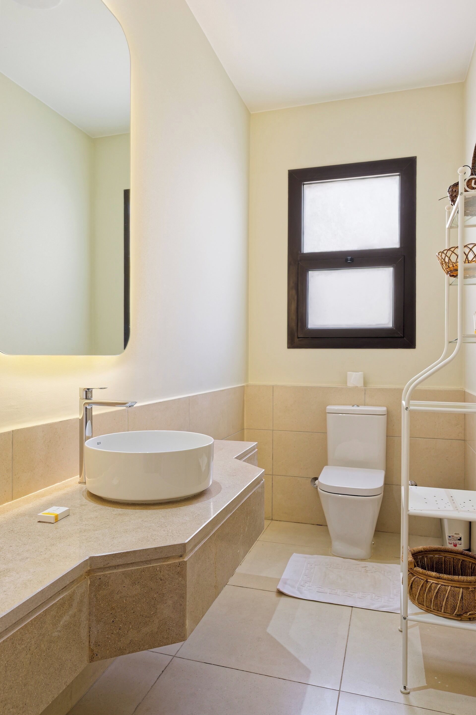 A modern bathroom with a round sink, a toilet, a window, and a mirror.