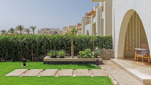 Ein modernes Gebäude mit weißer Fassade, einer überdachten Außenbestuhlung und einem gepflegten Garten mit Palmen und Sträuchern.