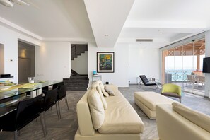 A modern living room with a glass dining table, a beige sofa, and a staircase leading to an upper floor. - VESTA - Luxury Apt - 3BR - Marina Soma Bay (Hurghada)