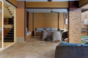 Ein modernes Interieur mit einer Couch, Korbstühlen, einem Deckenventilator und Blick auf eine Küche und einen Außenbereich.