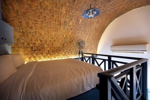 Ein Zimmer mit Backsteinwand, einem Bett mit weißer Bettwäsche, einem Deckenventilator und einer Klimaanlage.