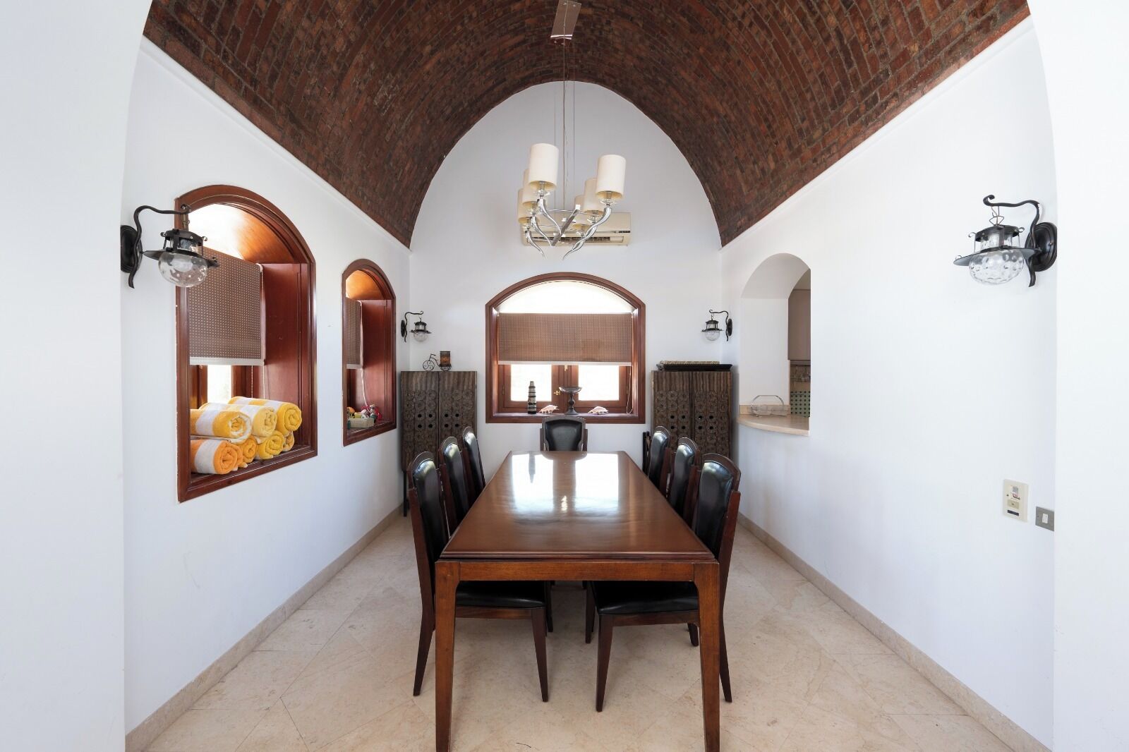 A dining area with a long wooden table, multiple chairs, and a brick ceiling.
