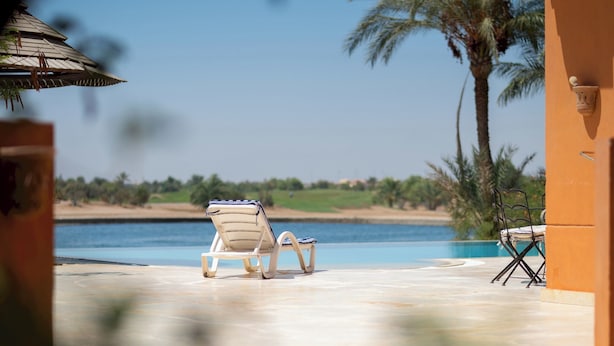 A poolside area with a lounge chair and a table, overlooking a body of water and a beach. - VESTA - Luxury Villa - 4BR - North Golf (II) (El Gouna)