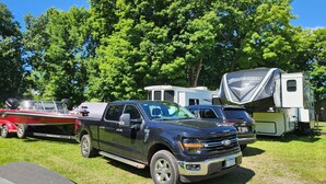 Ein schwarzer Pick-up-Truck steht auf einer Wiese, im Hintergrund sind ein Anhänger und ein Wohnmobil zu sehen.