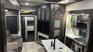 A compact kitchenette with a stove, oven, microwave, and a small dining area with a table and bench.
