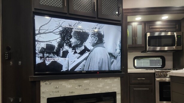 Eine moderne Küche mit Flachbildfernseher über einem Kamin, Edelstahlgeräten und einer gefliesten Spritzschutzwand.