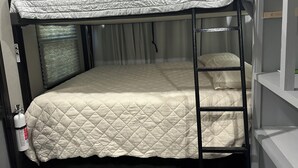 Ein Stockbett mit gesteppter Matratze, einer Stehleiter und einem Fenster mit Vorhängen.