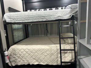 Una cama litera con colchón acolchado, una escalera y una ventana con cortinas.