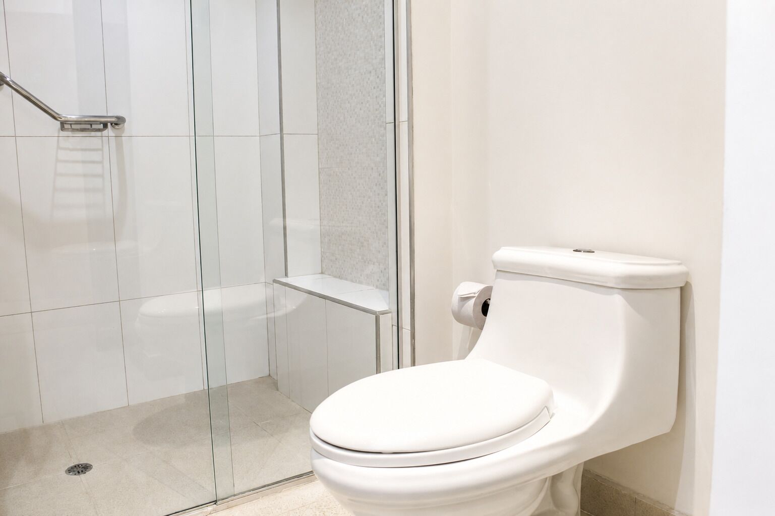 Egy modern fürőszoba, amelyben található egy WC, egy üvegajtós zuhanyzó és egy kapaszkodó.
