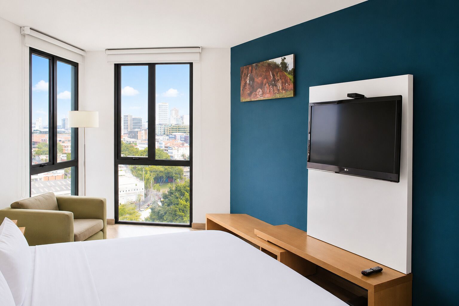 Hotelkamer met een bed, bureau, stoel, televisie en groot raam met uitzicht op de stad.