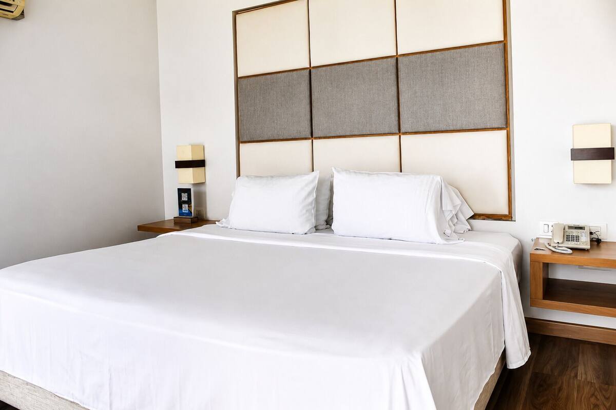 Habitación de hotel con una cama grande, una mesita de noche con teléfono y una lámpara fijada en la pared.