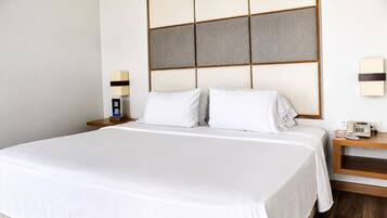 Quarto de hotel com uma cama grande, uma mesa de cabeceira com telefone e um candeeiro fixo na parede.