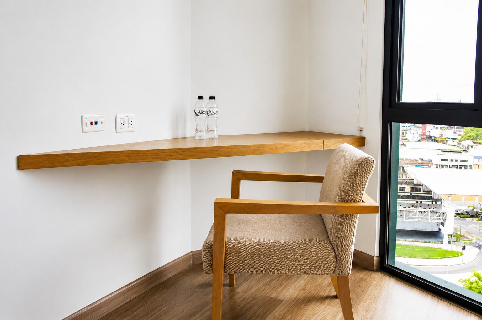 A corner room with a wooden chair, a shelf, and a window with a view of buildings.