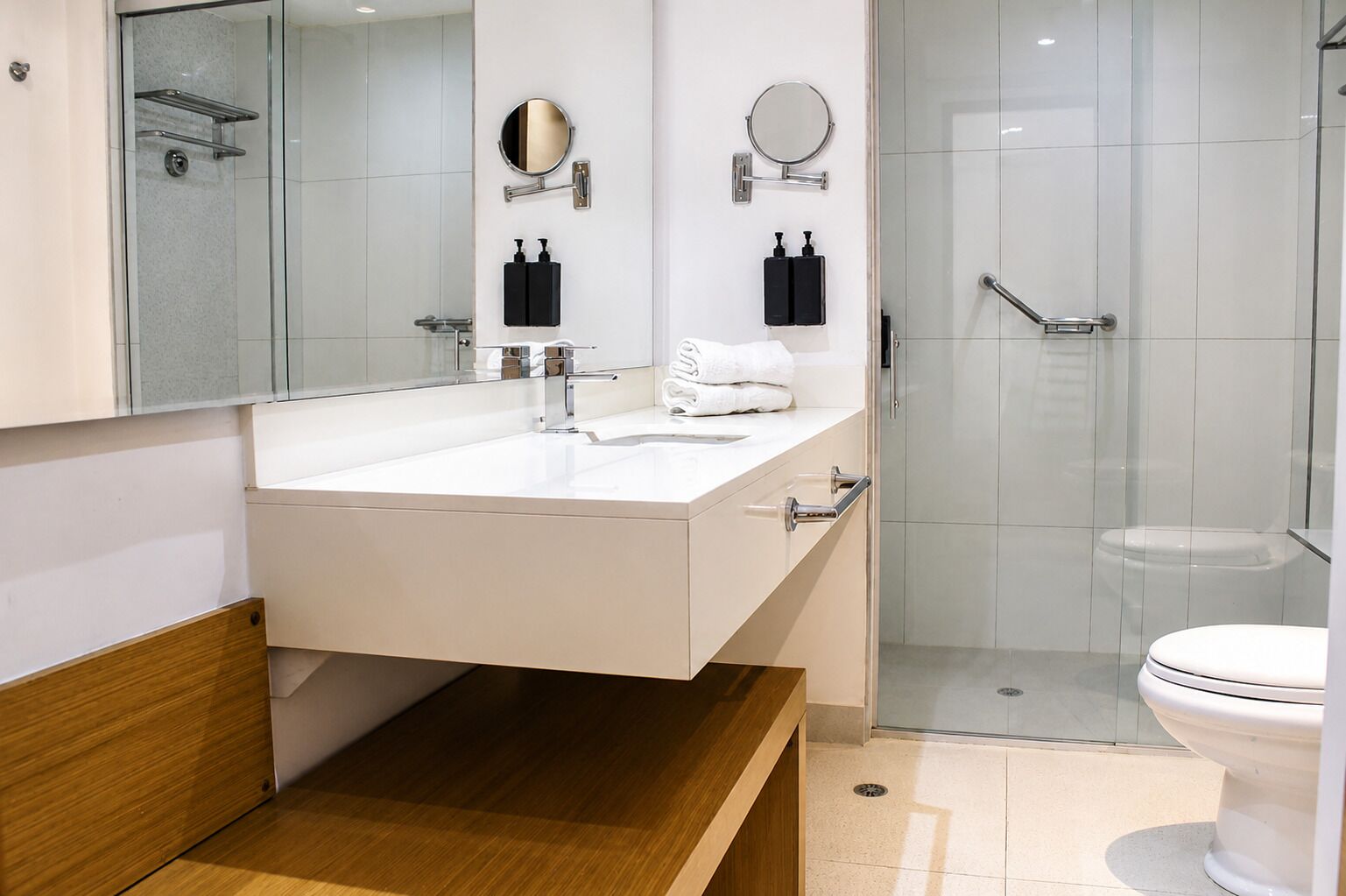 Un baño moderno con un lavamanos blanco, dos espejos, una cabina de ducha de cristal y un inodoro.