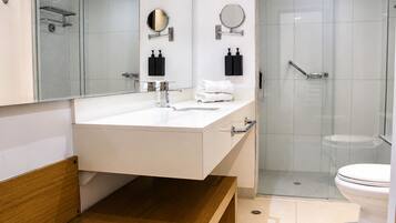 Un baño moderno con un lavamanos blanco, dos espejos, una cabina de ducha de cristal y un inodoro.