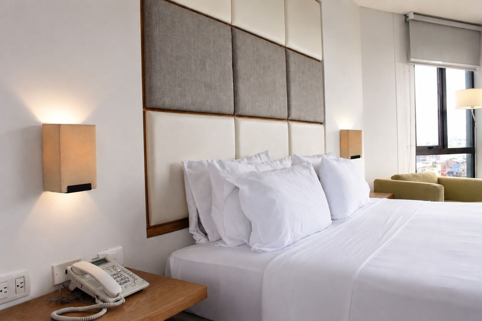 Une chambre d’hôtel avec un grand lit, un téléphone sur la table de chevet, un canapé et une tête de lit agrémentée d’appliques murales.