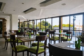 Un restaurant doté de nombreuses tables et chaises, de grandes fenêtres et offrant une vue sur la verdure environnante.