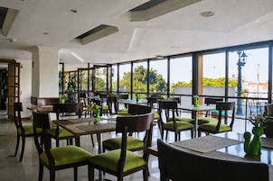 En restaurant med flere borde og stole, store vinduer og udsigt til grønne områder.
