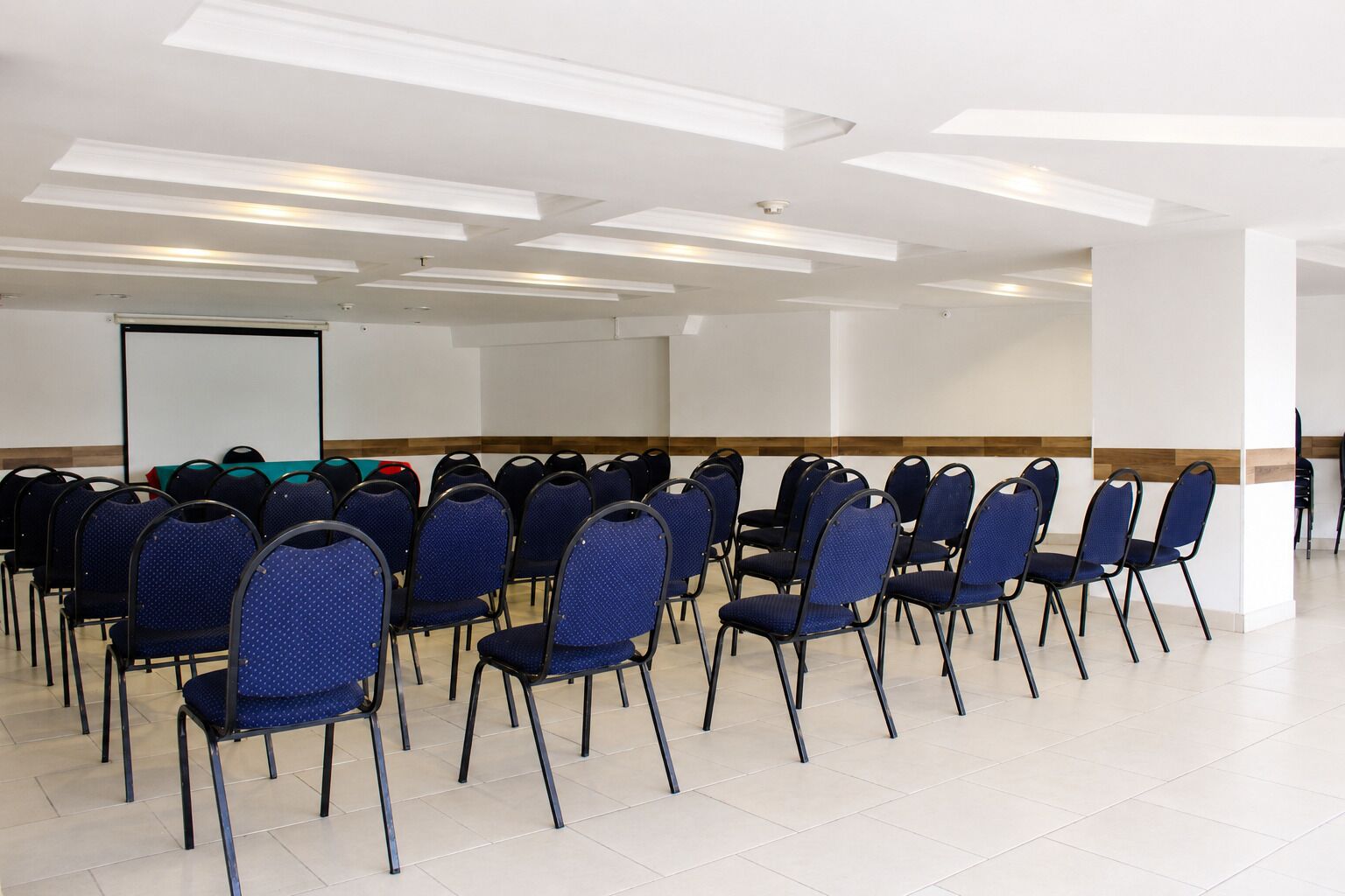 Un salón de conferencias con filas de sillas azules, una pizarra y suelo de baldosas.