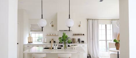Una cocina moderna con una isla central, luces colgantes y vistas al exterior.