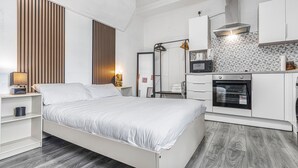A bedroom with a bed, bedside tables, a wardrobe, a mirror, and a kitchenette with a microwave, oven, and sink.