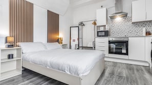 A bedroom with a bed, bedside tables, a wardrobe, a mirror, and a kitchenette with a microwave, oven, and sink.