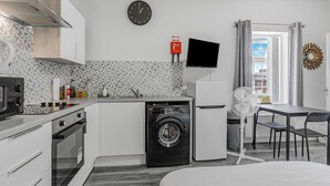 A compact kitchen with a washing machine, a flat-screen TV, and a dining area with a table and chairs.