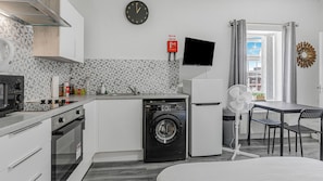 A compact kitchen with a washing machine, a flat-screen TV, and a dining area with a table and chairs. - Cosy & Comfortable City Centre Studio (Birmingham)