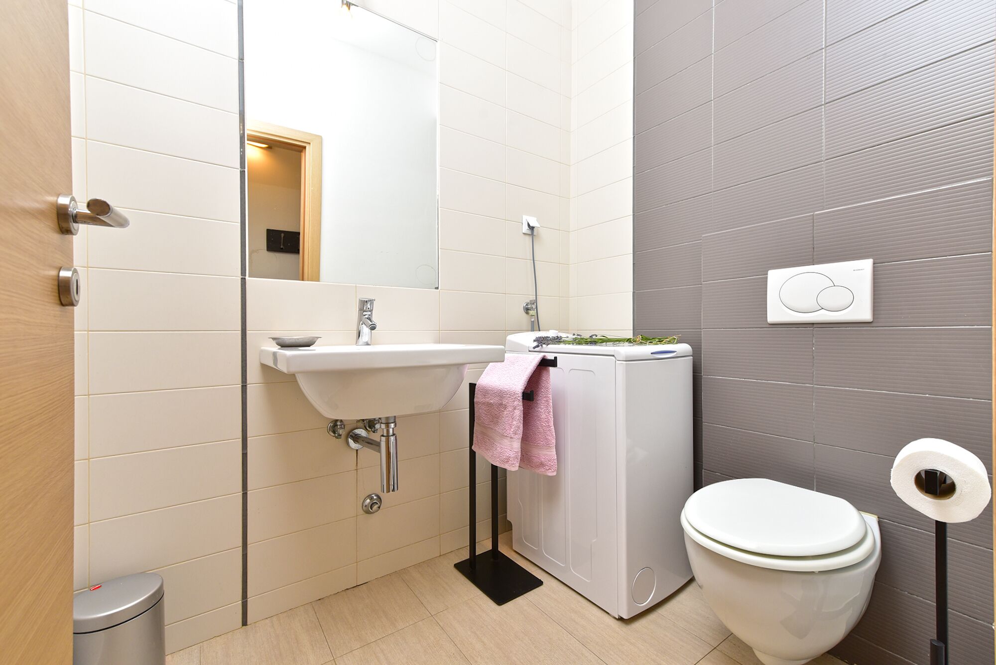 A modern bathroom with a sink, mirror, toilet, and a towel rack.