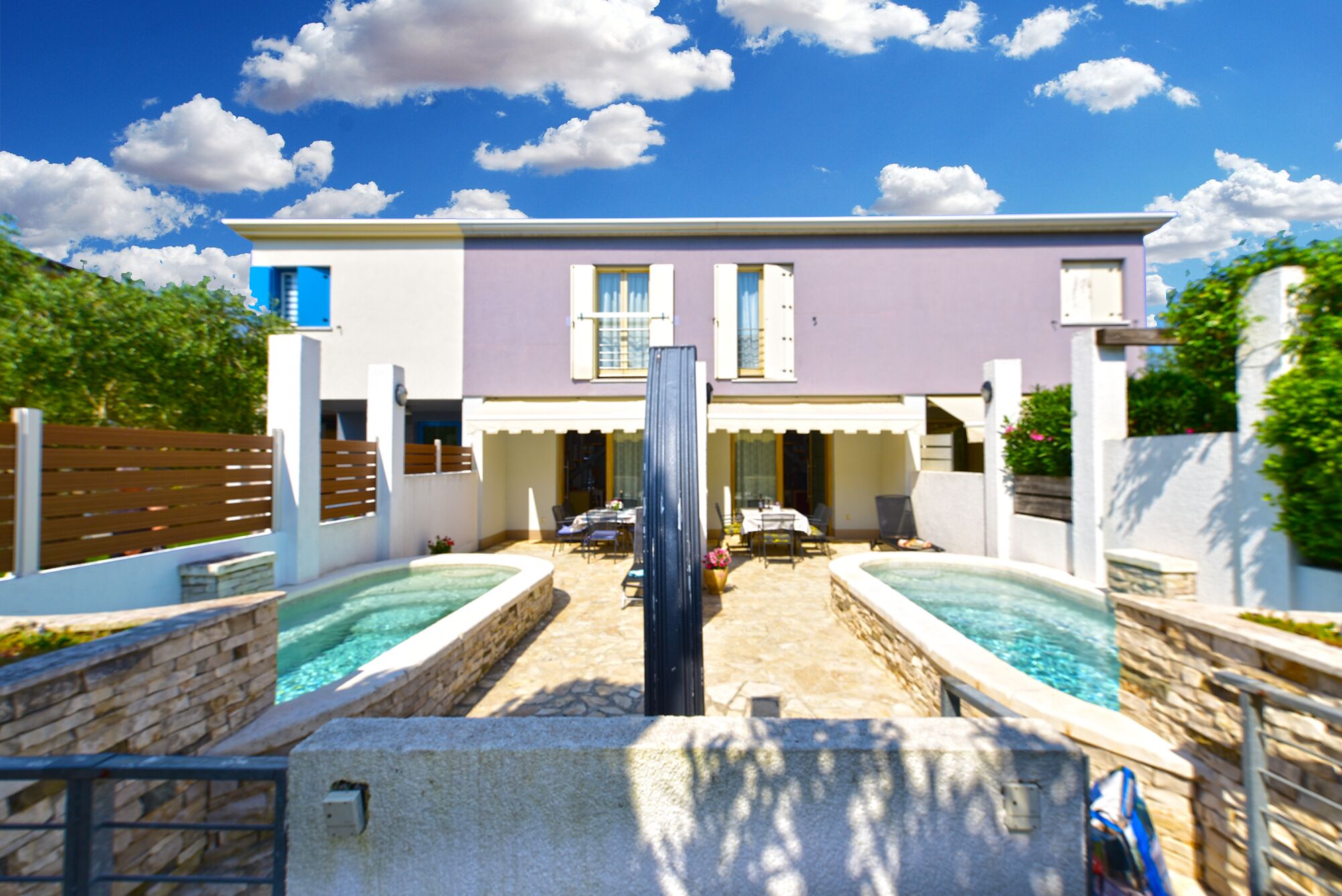 A two-story house with a swimming pool, outdoor seating, and a stone wall.