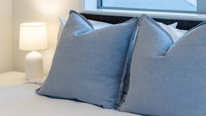 A bed with light blue pillows and a white lamp on a bedside table.